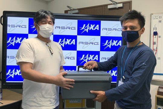 分配された試料を受け取る中村先生（左）（C）JAXA